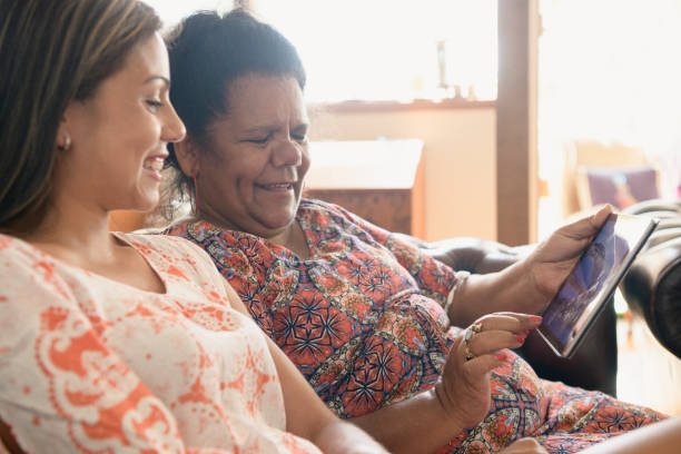 Mature Aboriginal woman touching screen as daughter watches and smiles